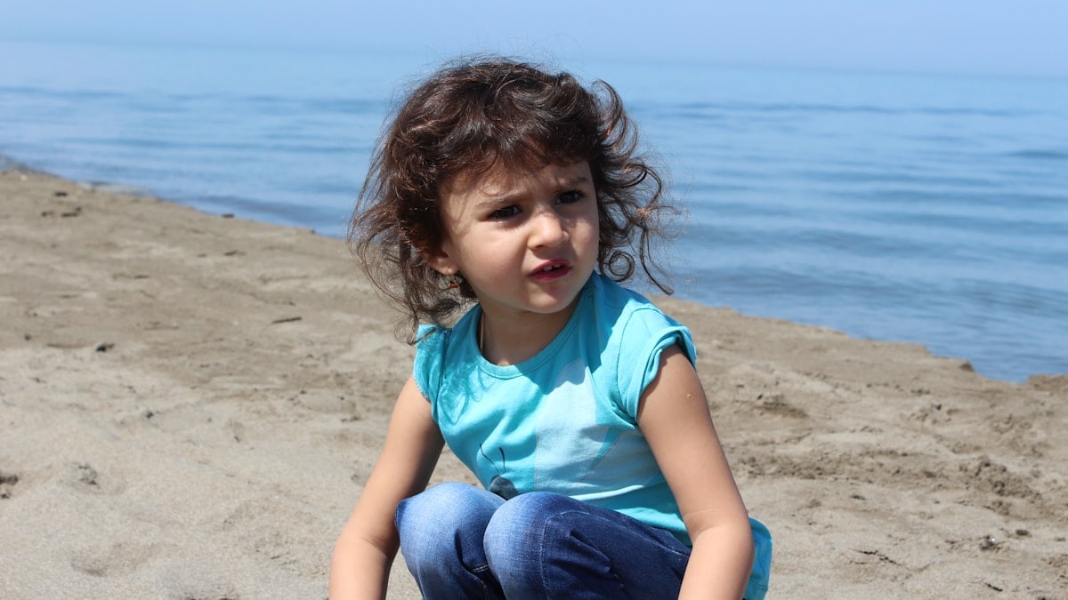 girl in teal shirt and blue denim jeans sitting on beach shore during daytime